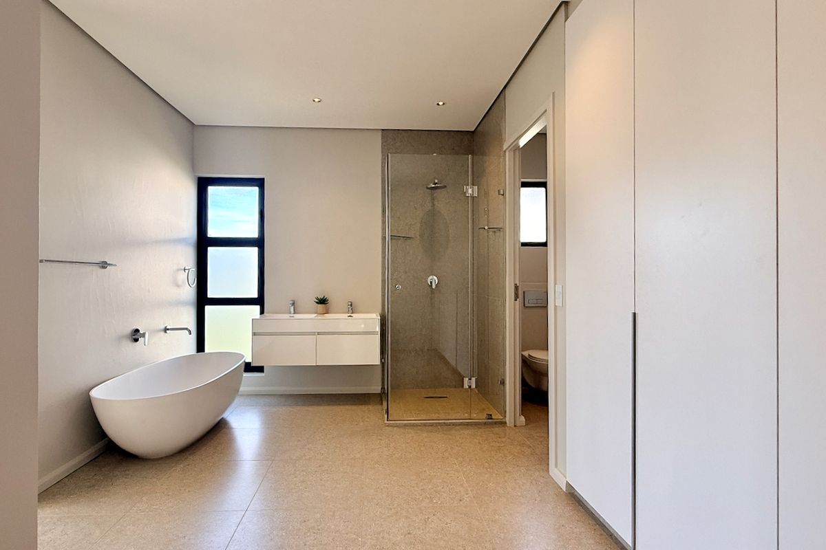 Modern, spacious bathroom featuring a sleek freestanding bathtub, wall-mounted double vanity, and a glass-enclosed shower with neutral tiled finishes.