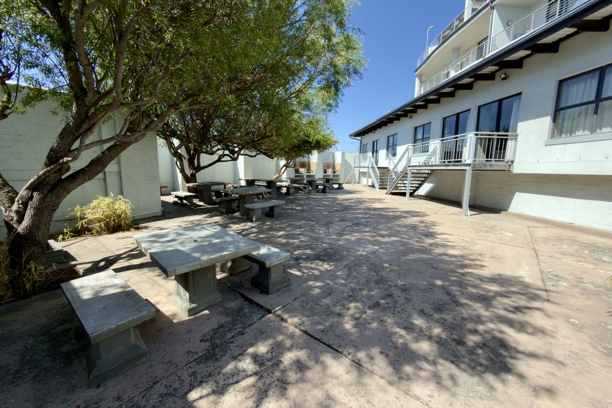 Spacious outdoor courtyard area featuring concrete paving, mature trees, and fixed stone seating, adjacent to the apartment building exterior.