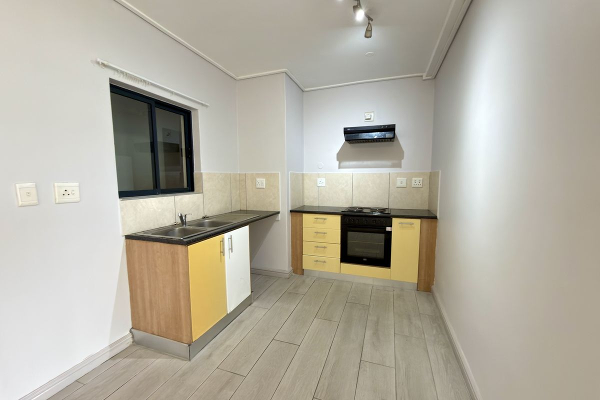 A functional kitchen featuring light wood-tone cabinetry, a built-in oven with extractor fan, tiled splashbacks, and modern wood-look floor tiles.