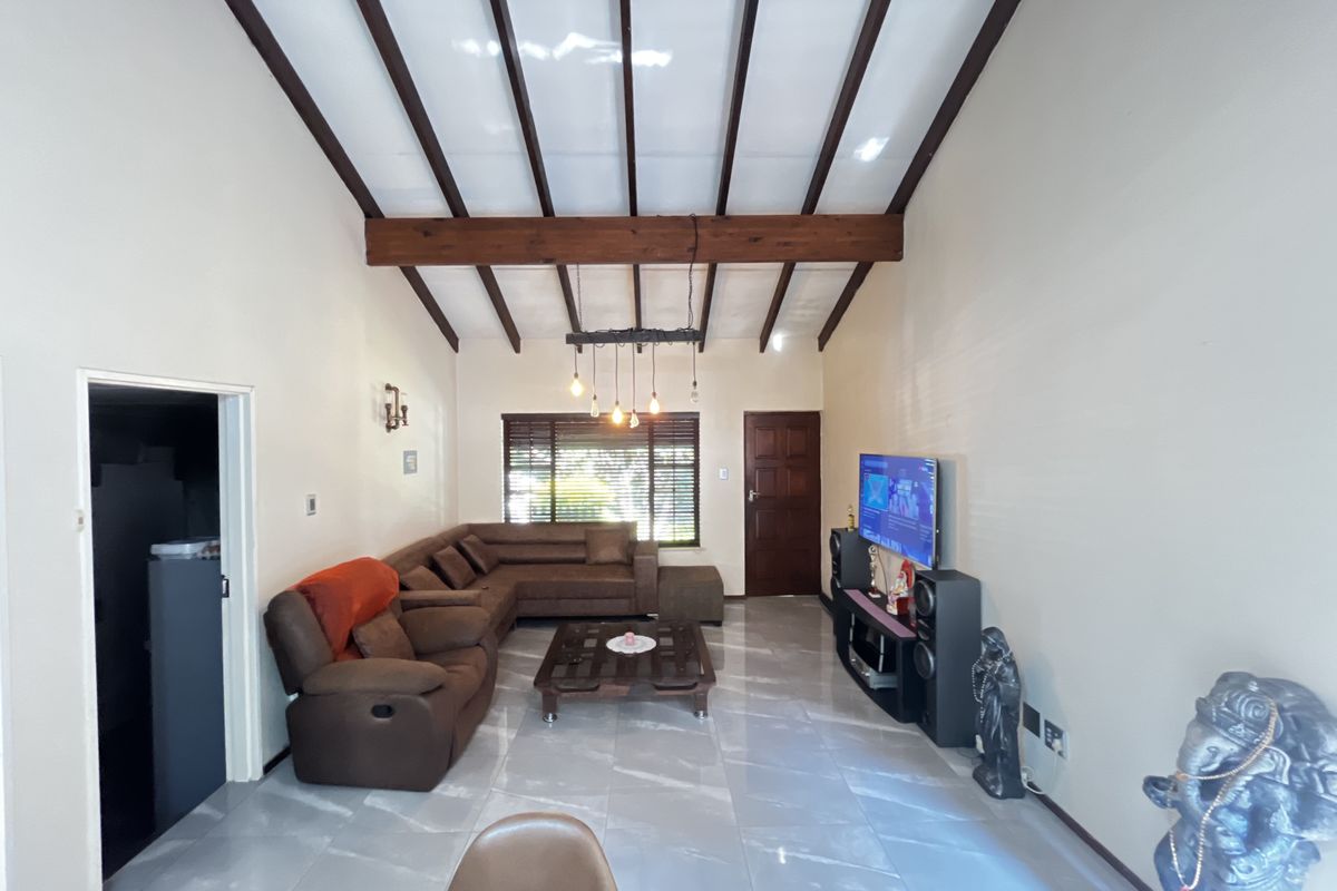 Spacious living room featuring high vaulted ceilings with exposed timber beams, large format floor tiles, and natural light through venetian blinds.