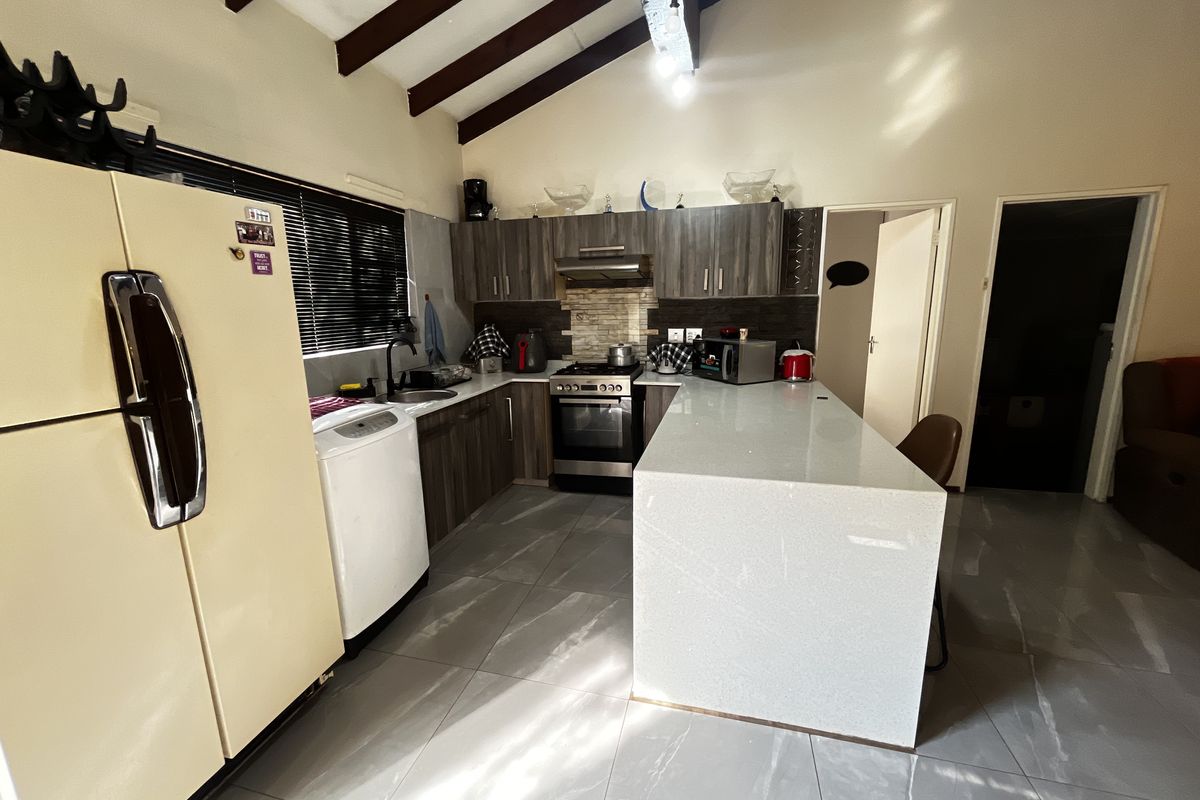 Modern kitchen featuring a large quartz island, vaulted ceilings with exposed timber beams, and contemporary cabinetry with integrated stainless steel appliances.
