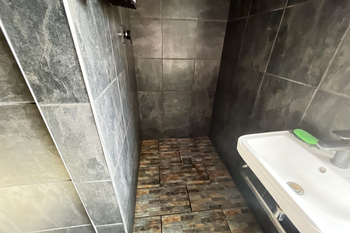 A compact bathroom featuring dark slate-style wall tiles, textured floor tiles, and a modern wall-mounted basin.