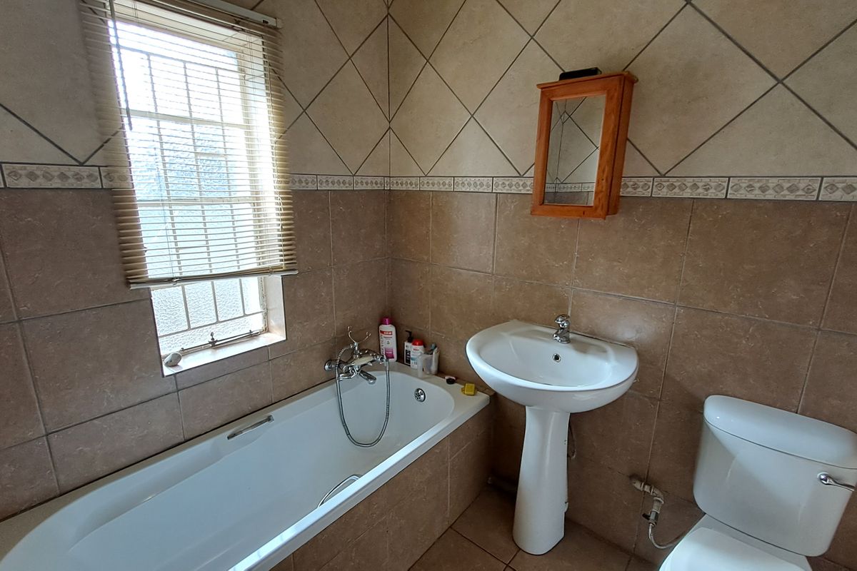 A functional bathroom featuring a pedestal washbasin, bathtub, and toilet, finished with neutral wall and floor tiling.
