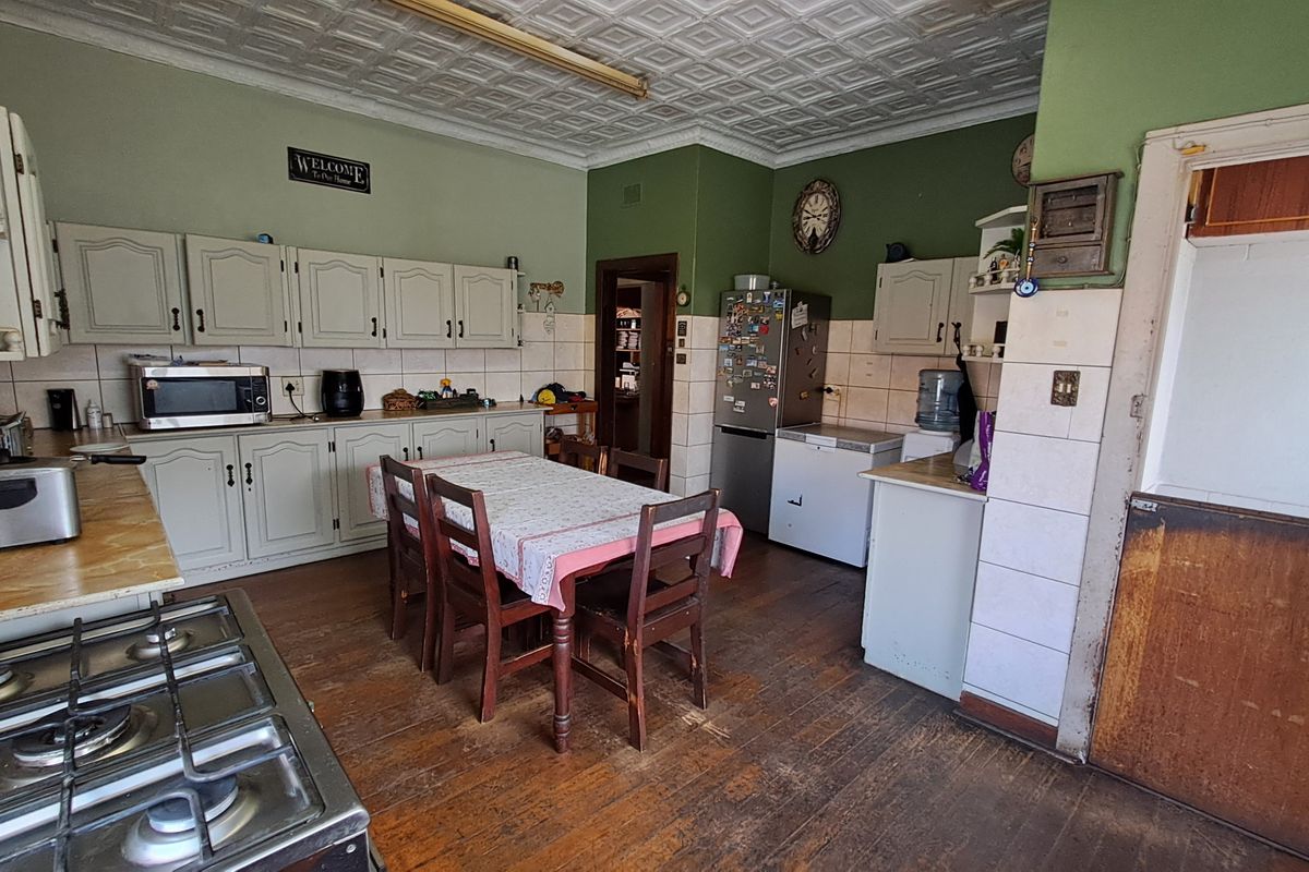 A spacious kitchen featuring traditional pressed metal ceilings, timber flooring, and extensive built-in cabinetry with a gas hob and tiled backsplash.