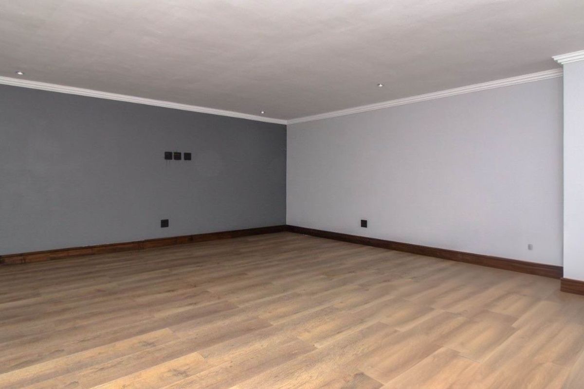 A spacious, empty living room featuring modern laminate flooring, recessed downlights, and clean, neutral-toned walls with decorative cornice detailing.