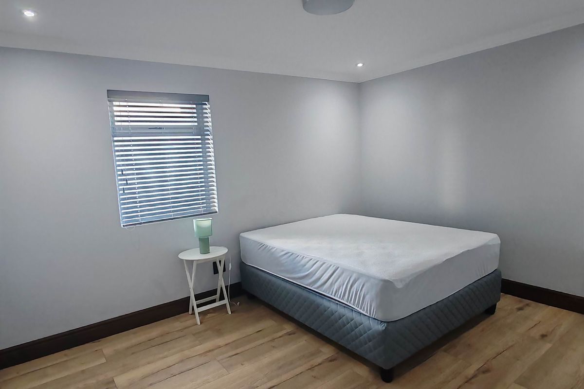 A bright, neutral bedroom featuring modern laminate wood flooring, recessed downlighting, and fitted window blinds.