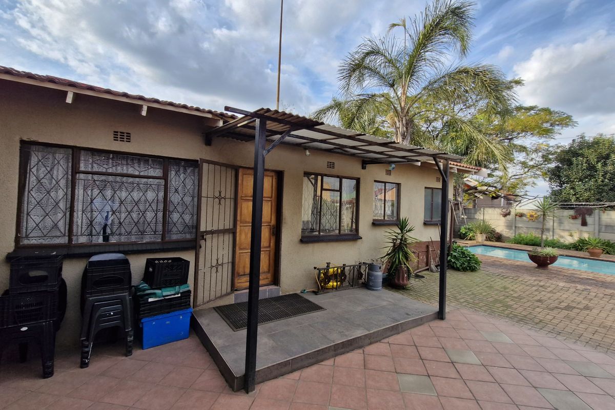 Rear exterior view featuring a tiled patio with a metal pergola, paved courtyard area, and a swimming pool.