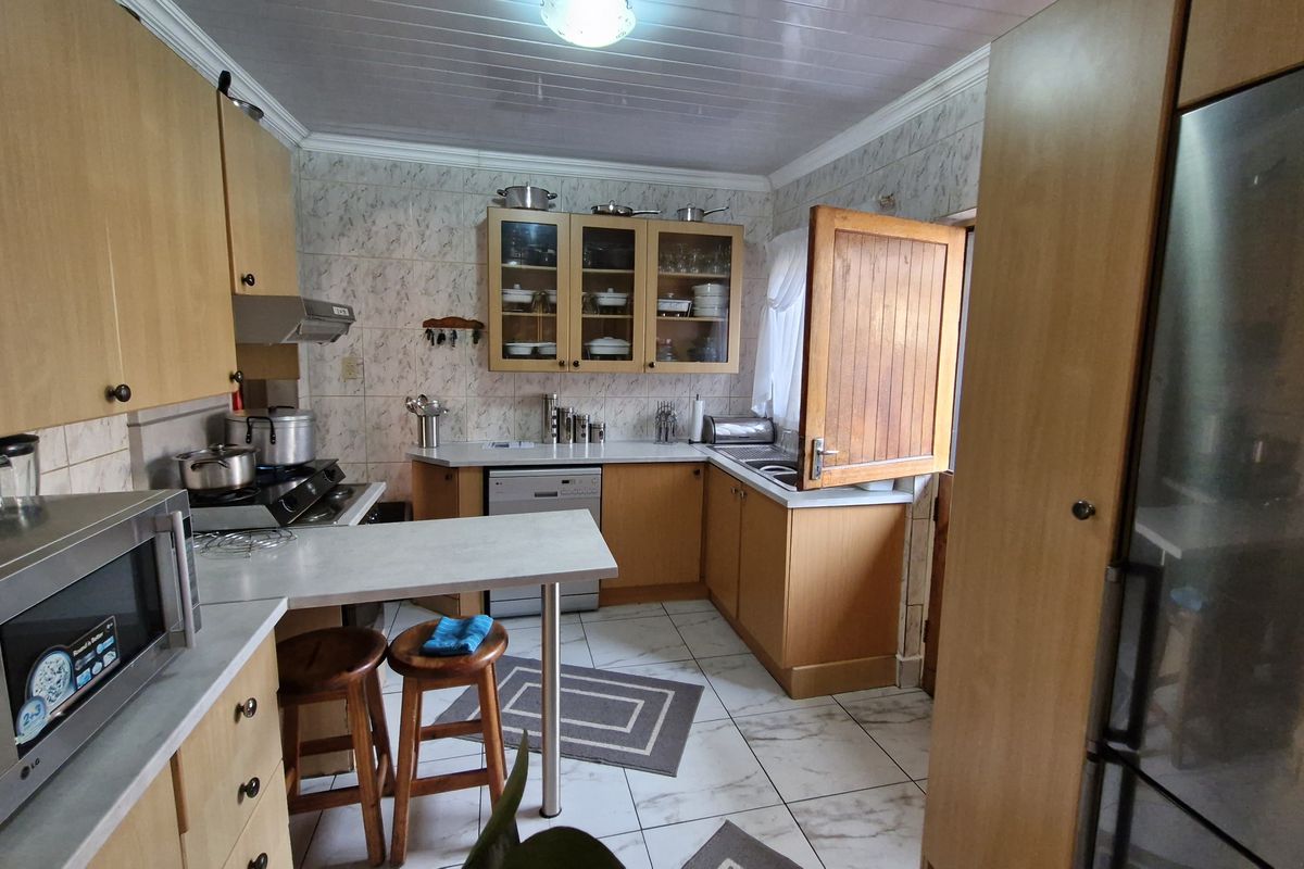 A functional kitchen featuring wood-tone cabinetry, tiled backsplash, integrated appliances, and tiled flooring, offering a practical layout for daily meal preparation.