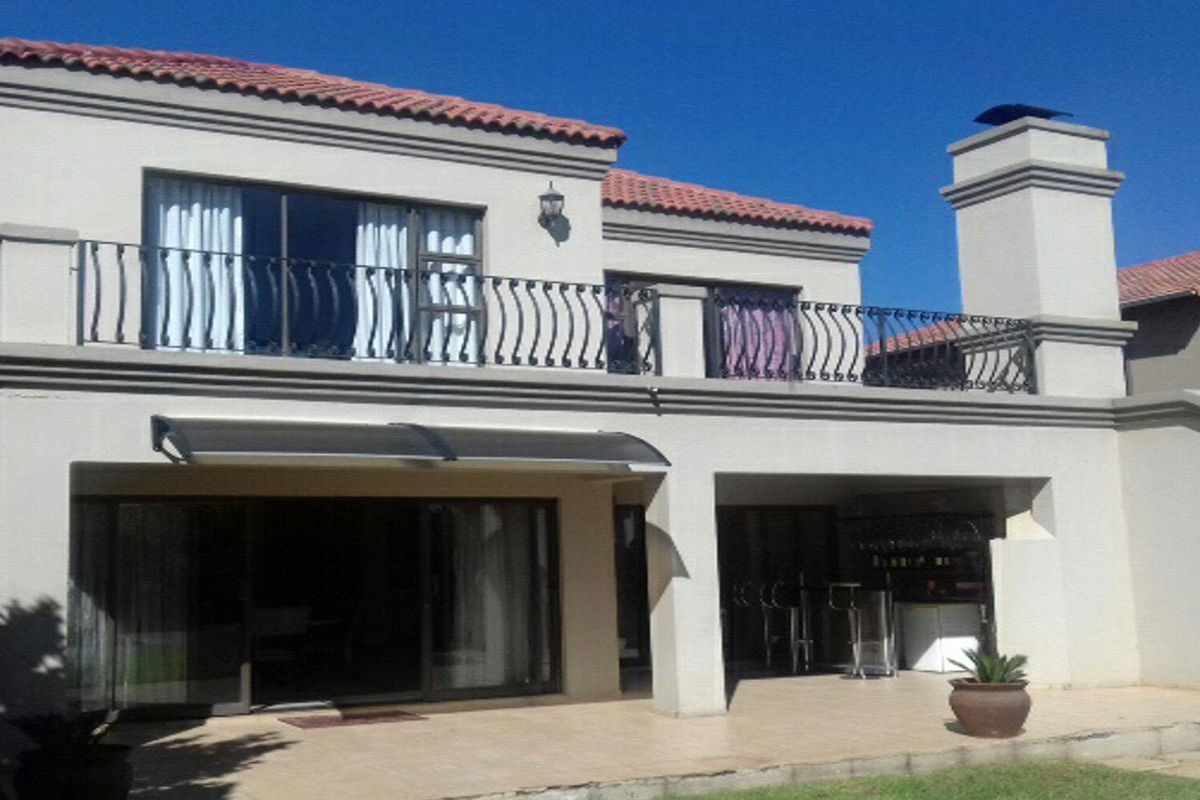 Rear elevation of a two-story apartment featuring a covered patio, upper-level balcony with wrought iron railings, and terracotta roof tiles.