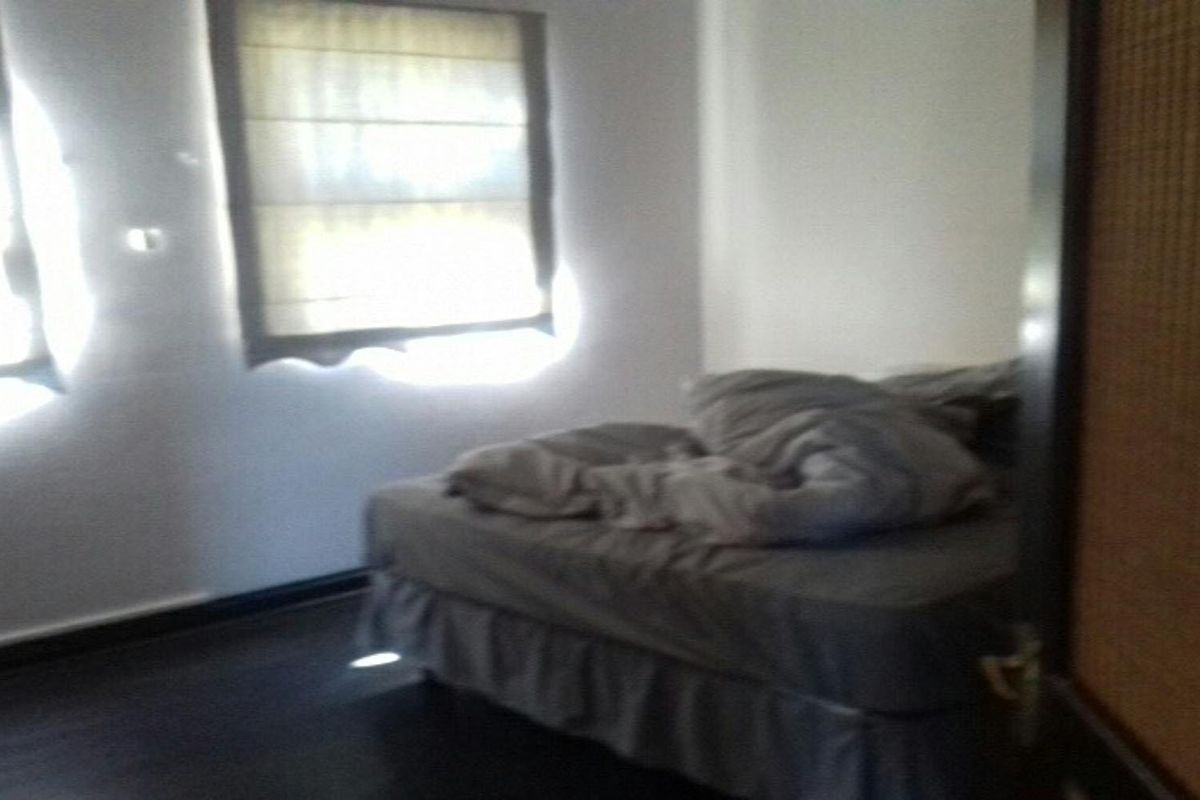 A bedroom featuring dark wood flooring and window blinds, currently presented with a bed.