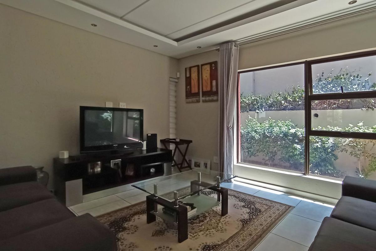 A comfortable living room featuring tiled flooring, a recessed ceiling design, and a large window providing natural light and a view of the garden.