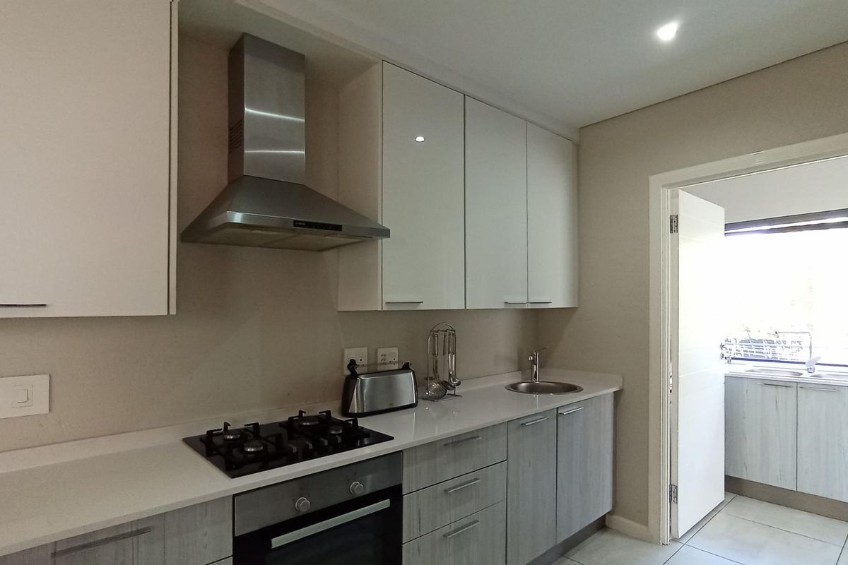 Modern kitchen featuring glossy cabinetry, stone countertops, a gas hob, built-in oven, and stainless steel extractor fan, with an adjacent scullery area.