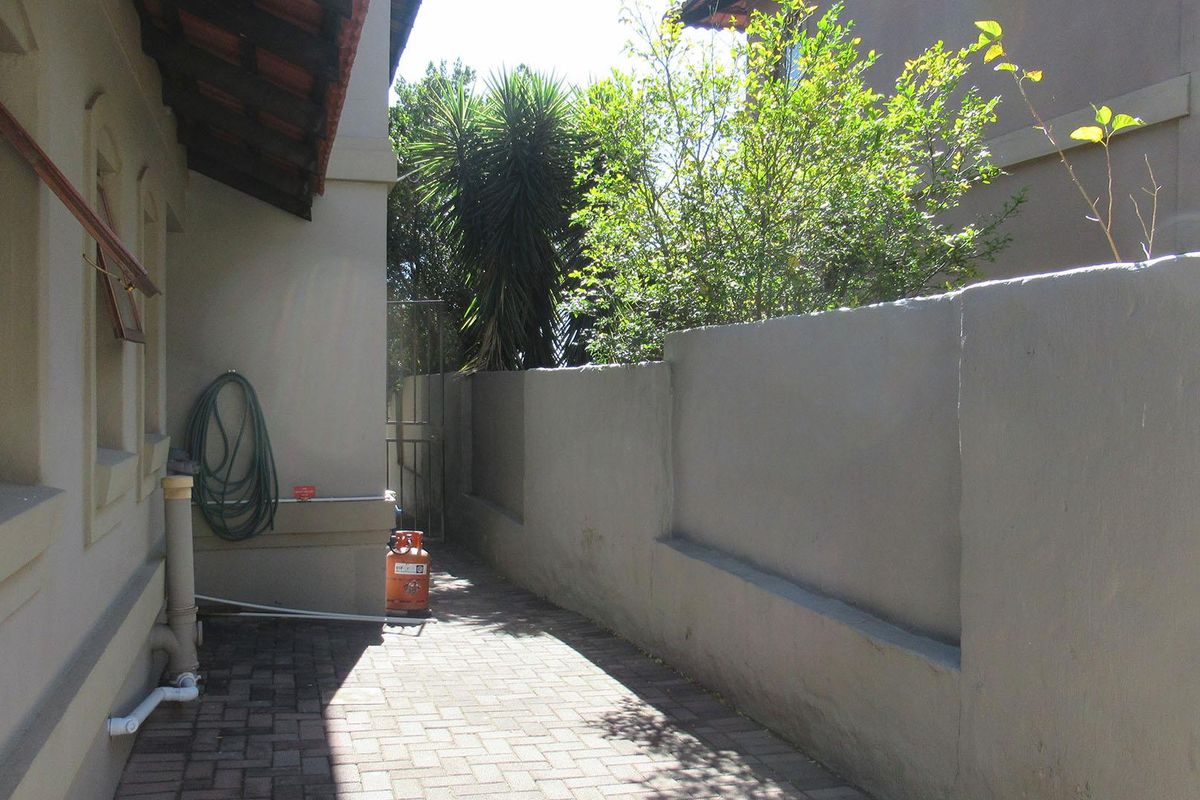 A side exterior walkway featuring paved flooring, a solid boundary wall, and external plumbing fixtures along the side of the house.