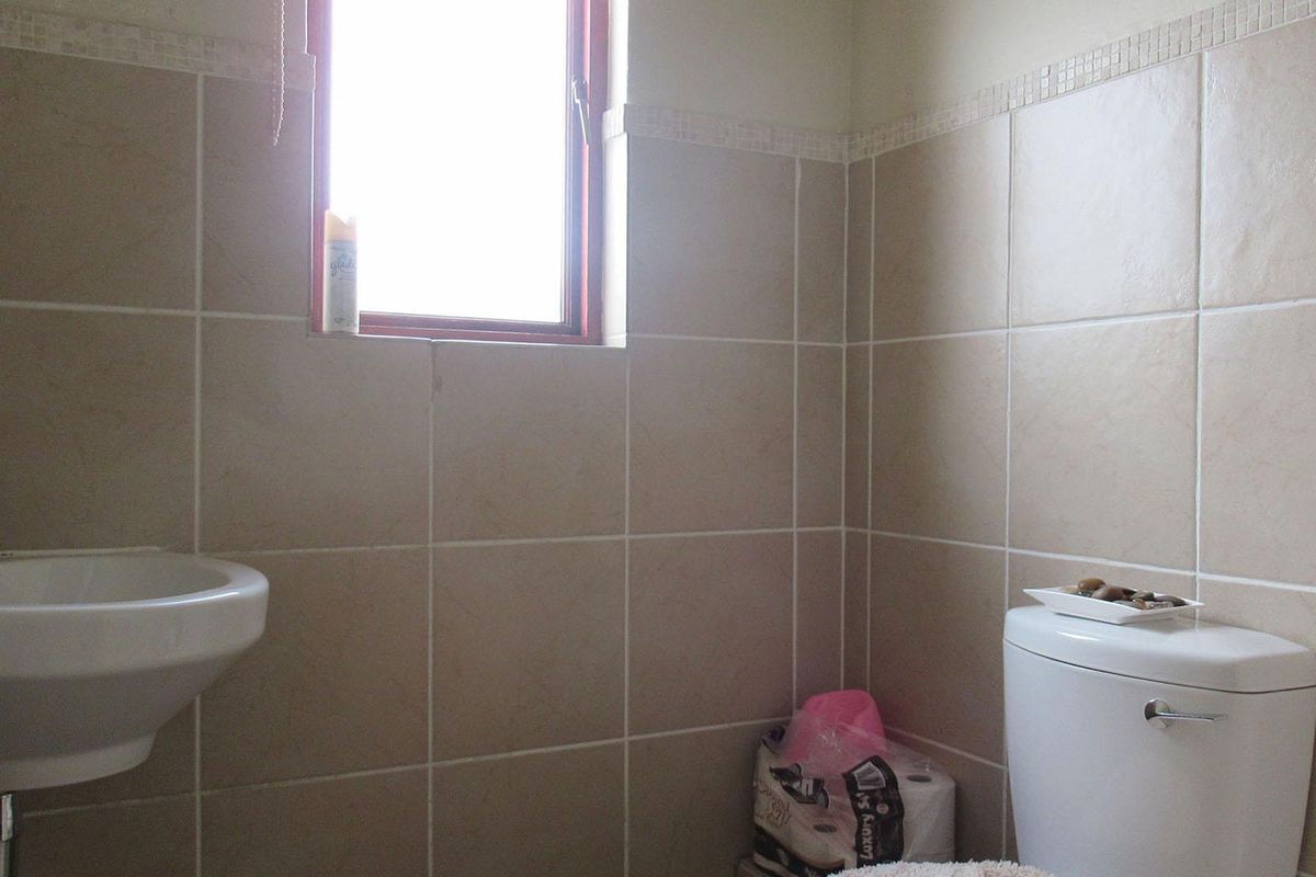 A functional bathroom featuring neutral wall tiles with a mosaic border, a wall-mounted basin, and a standard toilet.