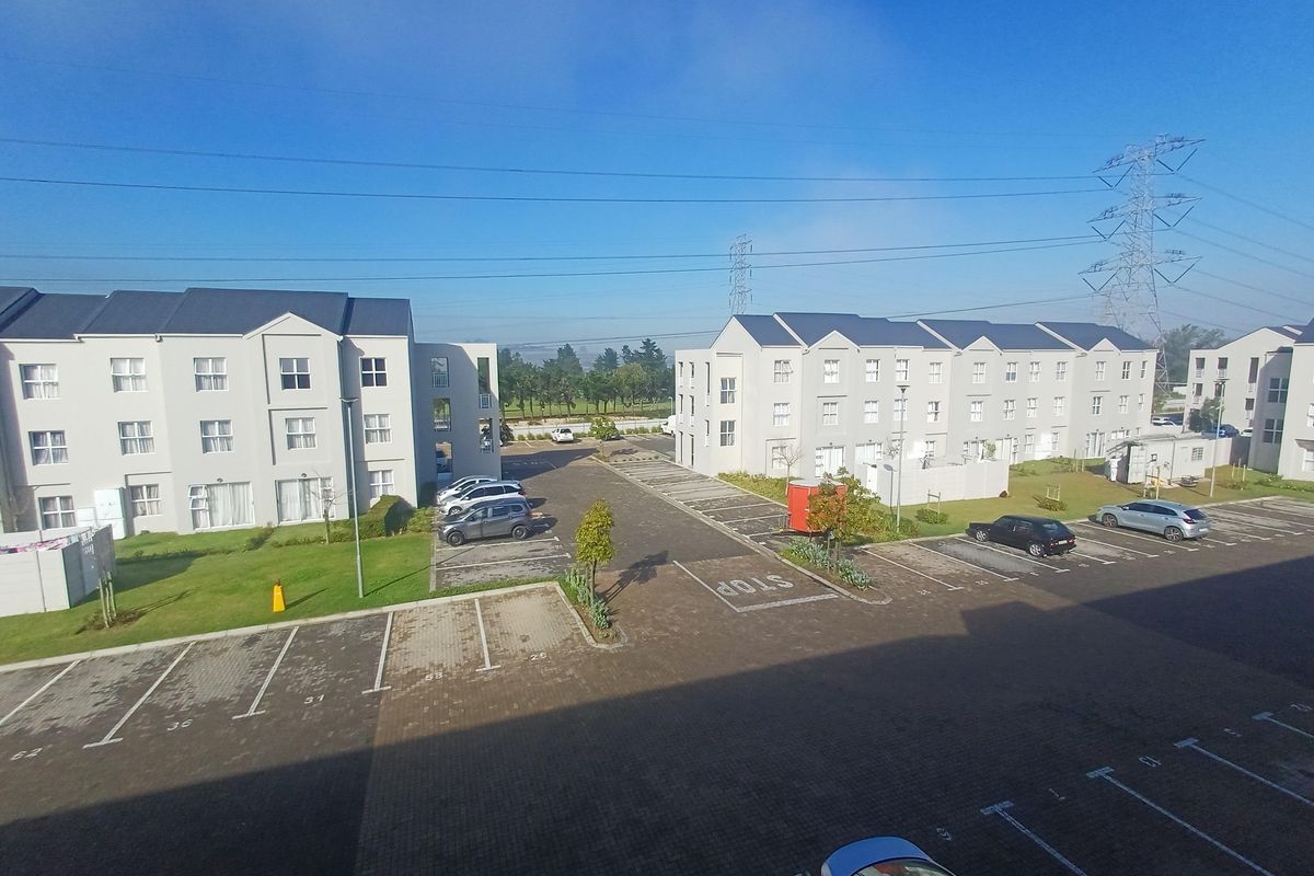An elevated view of the apartment complex grounds, featuring paved parking areas, landscaped lawns, and multi-story residential buildings.