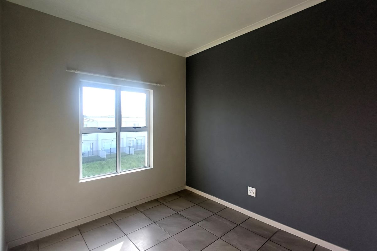 A bright, empty bedroom featuring neutral and dark accent walls, tiled flooring, and a window providing natural light.