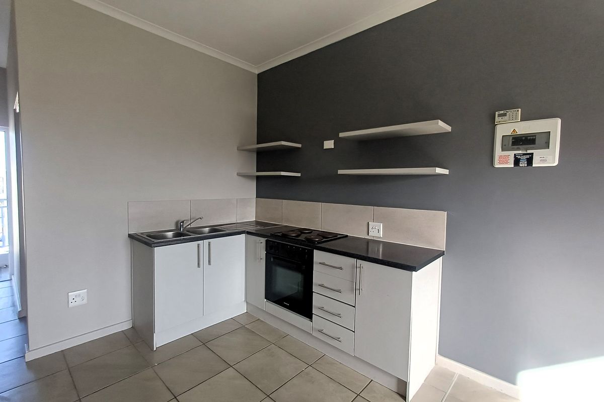 A compact kitchen featuring built-in cabinetry, a stainless steel sink, an integrated oven and hob, and floating wall shelves.