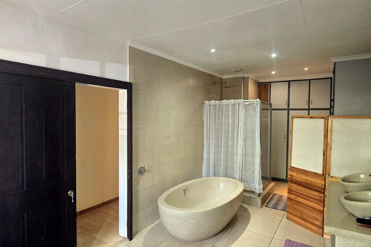 Spacious bathroom featuring a freestanding bathtub, separate shower enclosure, double vanity with vessel sinks, and ample built-in storage cupboards.