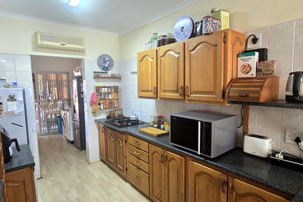 A functional kitchen featuring traditional wooden cabinetry, laminate countertops, a gas hob, and a tiled backsplash, with an adjacent laundry area visible.