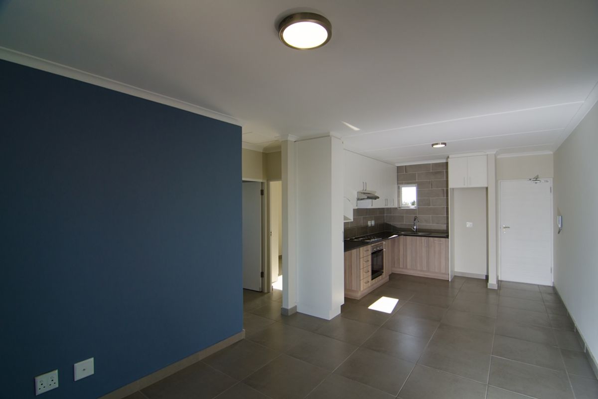 Open-plan living area featuring a modern kitchen with built-in cabinetry, oven, hob, and extractor fan, complemented by neutral floor tiling.
