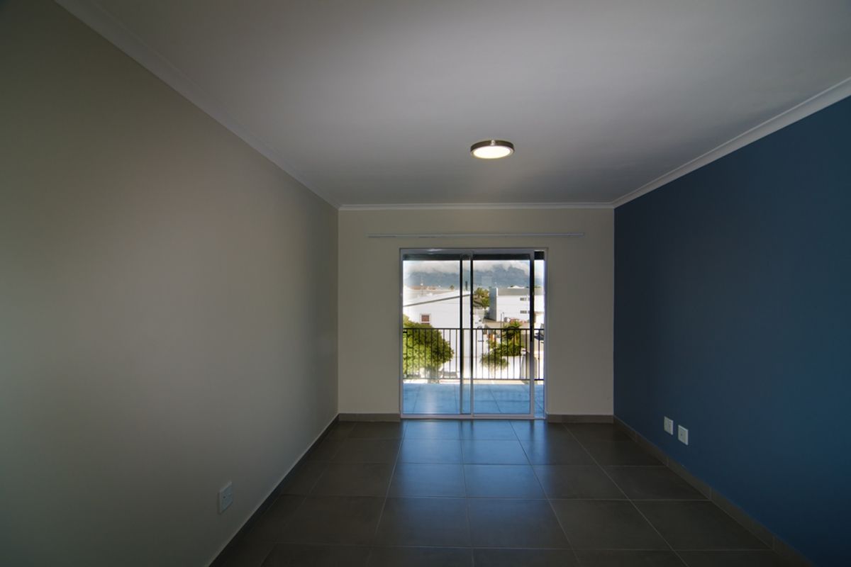 An empty living room featuring tiled flooring, a blue accent wall, and sliding glass doors leading to a balcony with an outdoor view.
