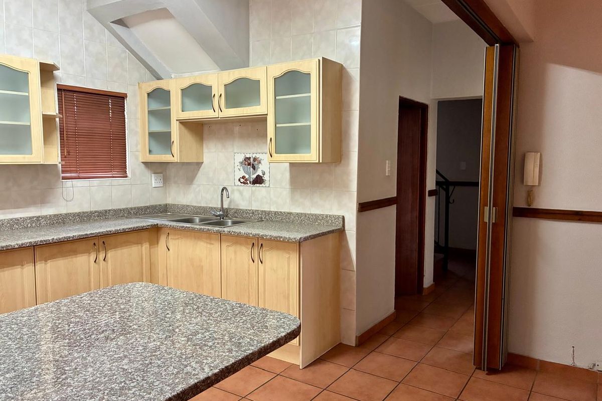 A functional kitchen featuring laminate cabinetry, granite countertops, a double basin sink, and tiled flooring, offering a practical layout for culinary activities.