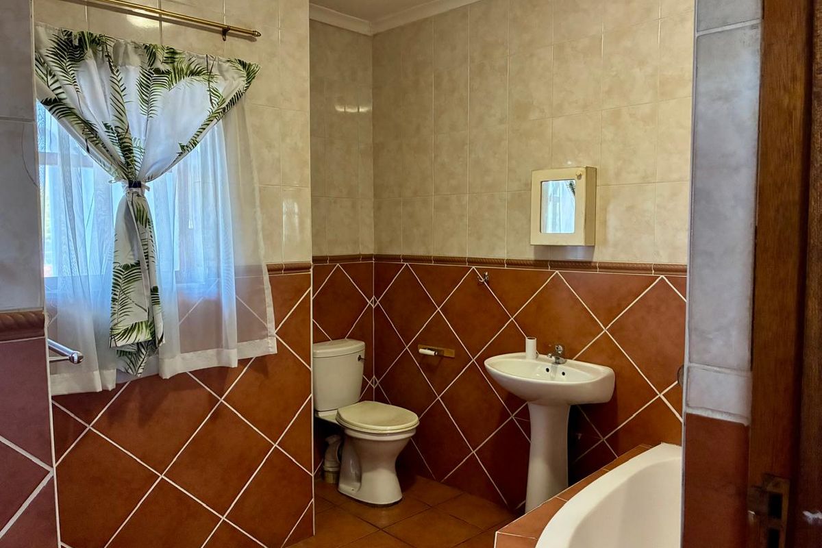 A functional bathroom featuring a pedestal sink, toilet, and bathtub with classic two-tone ceramic wall tiling.