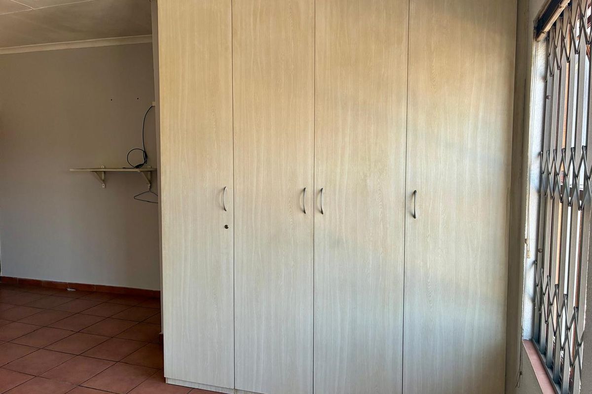 A bedroom featuring built-in wooden cupboards, tiled flooring, and security bars on the window.