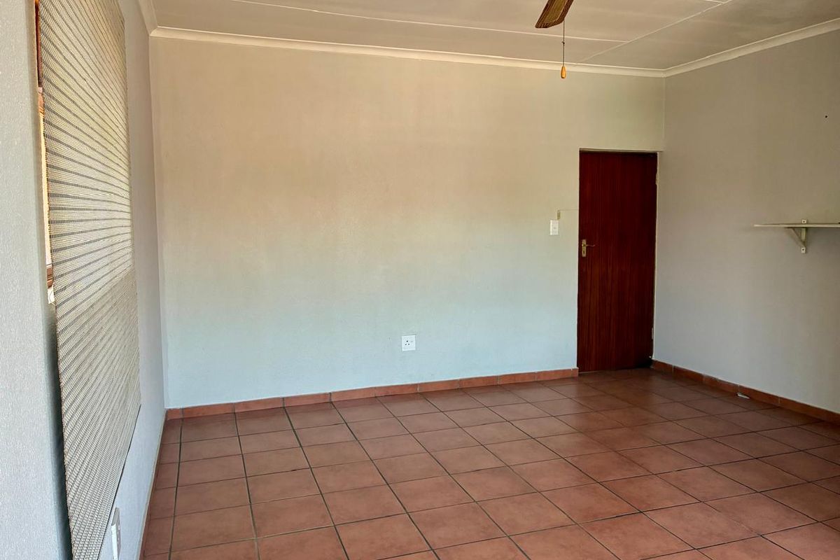 An empty living room featuring terracotta floor tiles, a ceiling fan, and a timber door, offering a blank canvas for interior design.