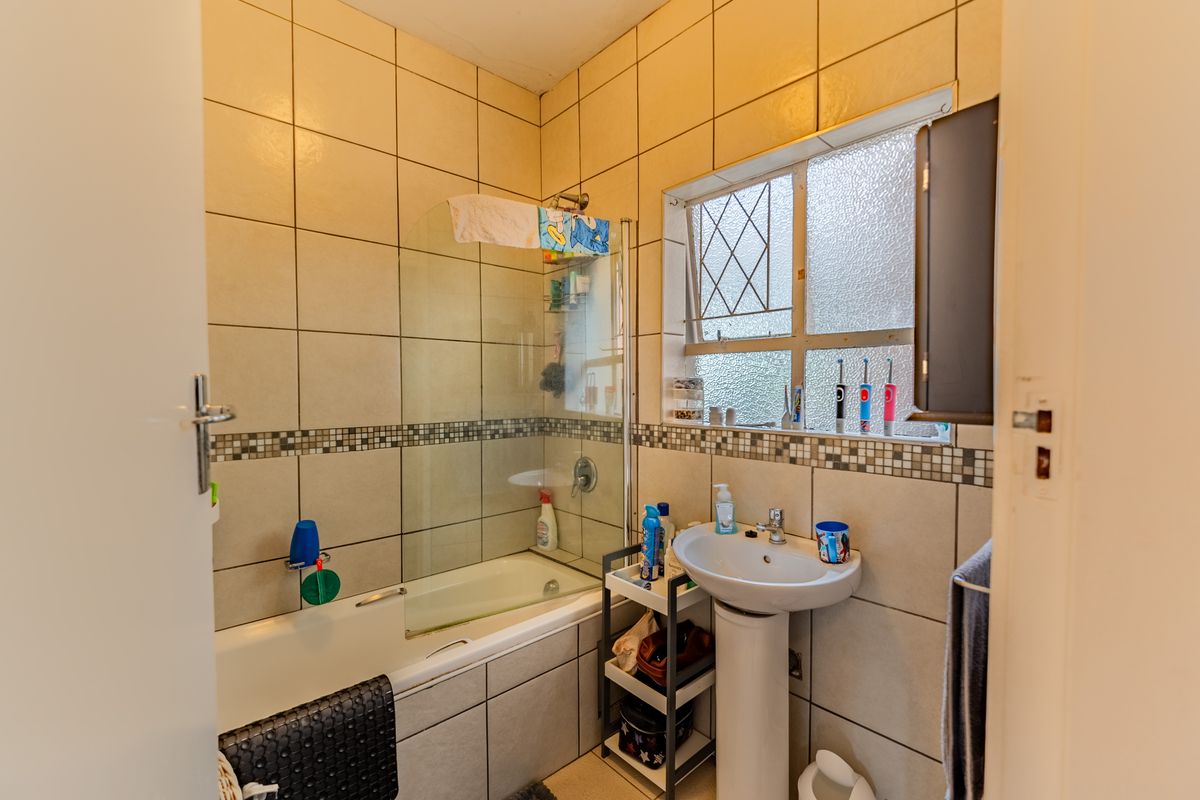 A compact bathroom featuring a pedestal basin, a bathtub with a glass shower screen, and full-height wall tiling.