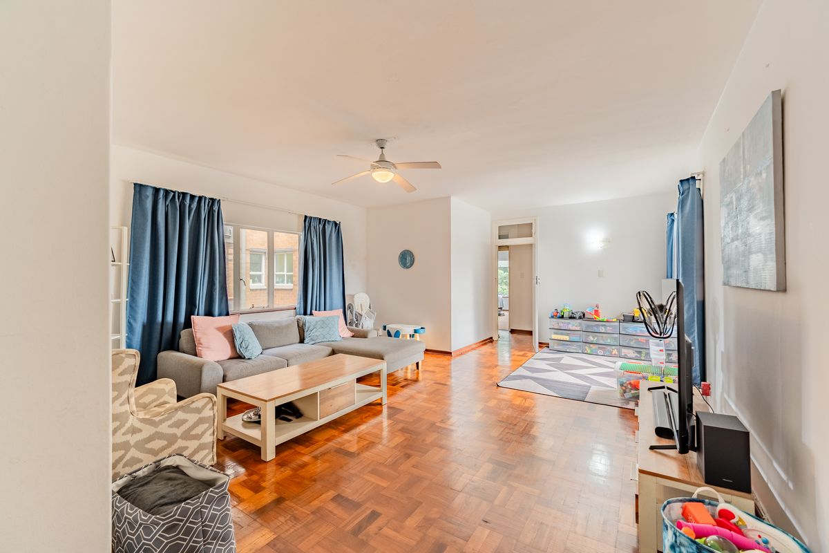 Spacious living room featuring classic parquet flooring, a ceiling fan, and large windows that provide ample natural light.