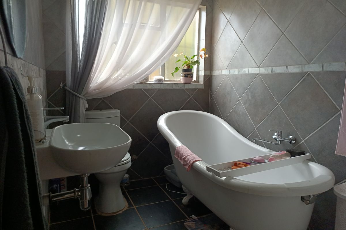 A well-maintained bathroom featuring a classic freestanding bathtub, wall-mounted basin, and neutral-toned ceramic wall and floor tiling.