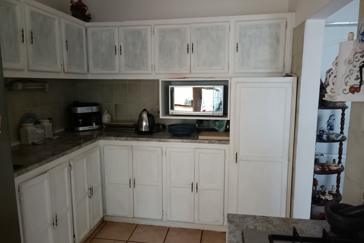 A functional kitchen featuring built-in cabinetry, laminate countertops, tiled backsplash, and a built-in microwave, offering potential for cosmetic updates.
