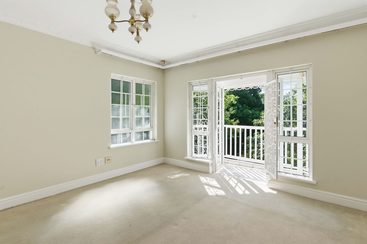 Bright and spacious bedroom featuring neutral carpeting, crown molding, and direct access to a private balcony through classic french doors with security gates.