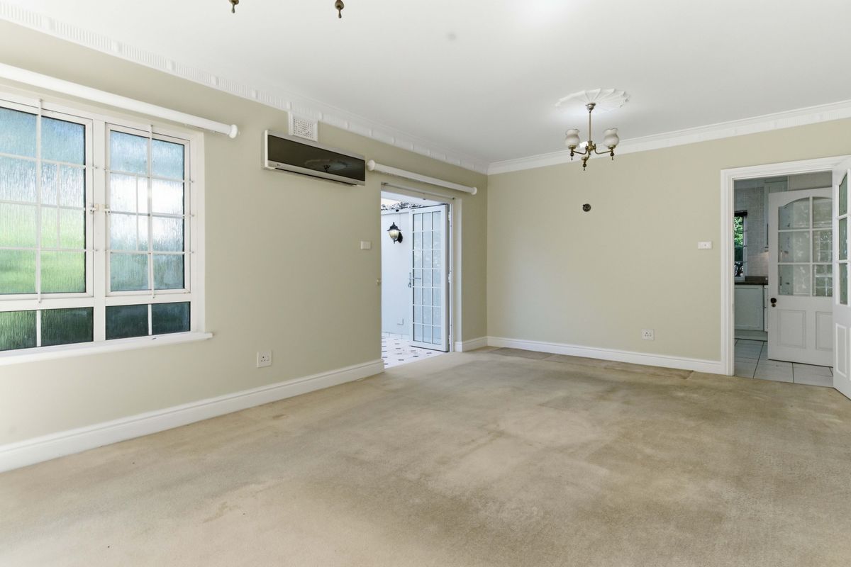 Spacious living room featuring crown molding, ceiling roses, an air conditioning unit, and access to an outdoor patio area through a glass-paneled door.