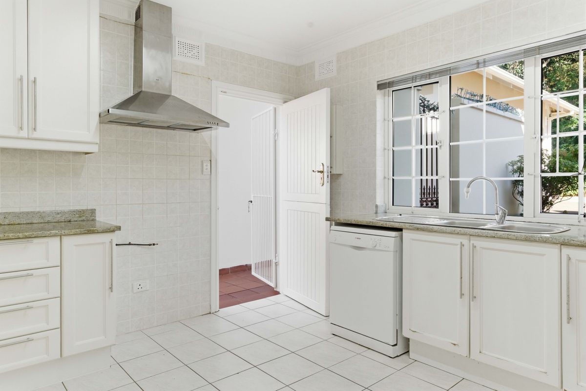 A functional kitchen featuring white cabinetry, granite countertops, a stainless steel extractor fan, and tiled finishes, with direct access to an exterior area.