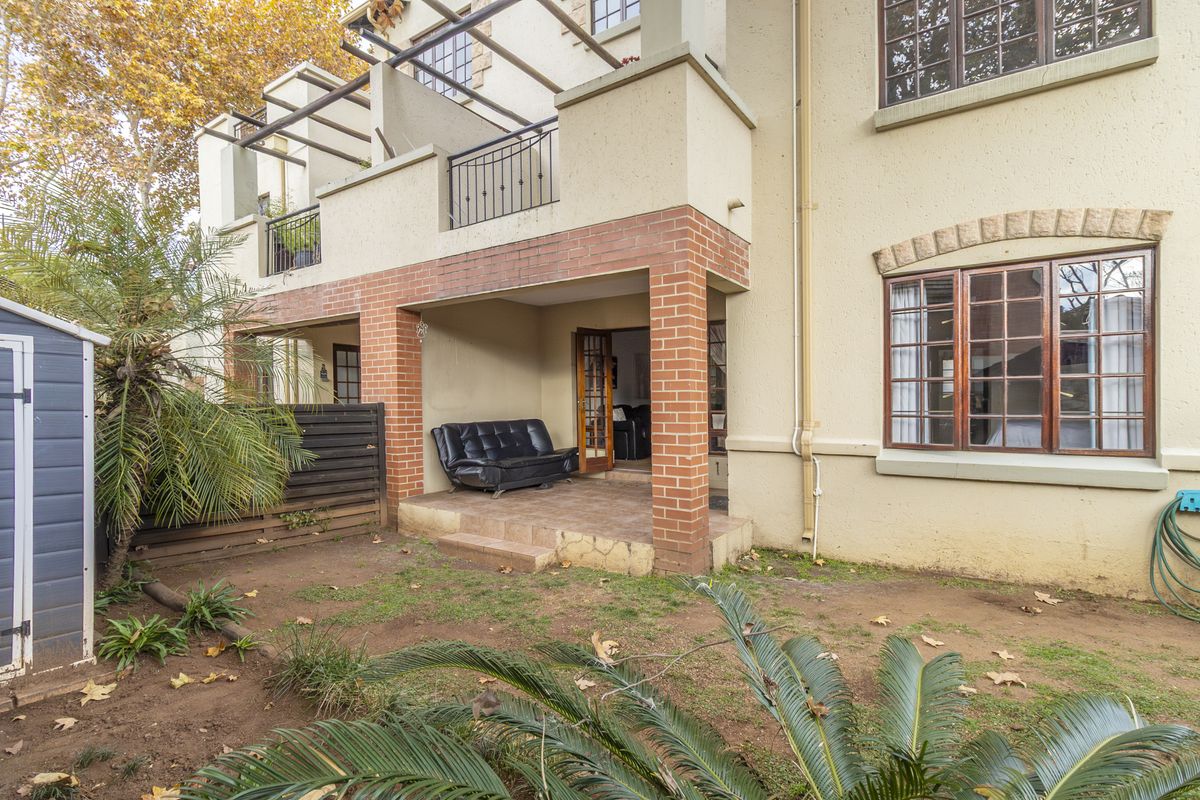 Rear view of the apartment featuring a covered patio with brick pillars, a timber pergola, and access to a small private garden area.