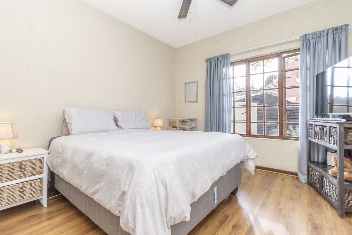 A well-lit bedroom featuring laminate flooring, a ceiling fan, and a timber-framed window overlooking the exterior.