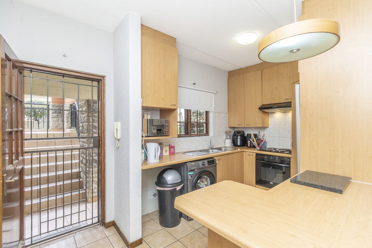 Functional kitchen featuring light wood cabinetry, built-in oven, hob, extractor fan, and tiled flooring, with direct access to an exterior entrance.