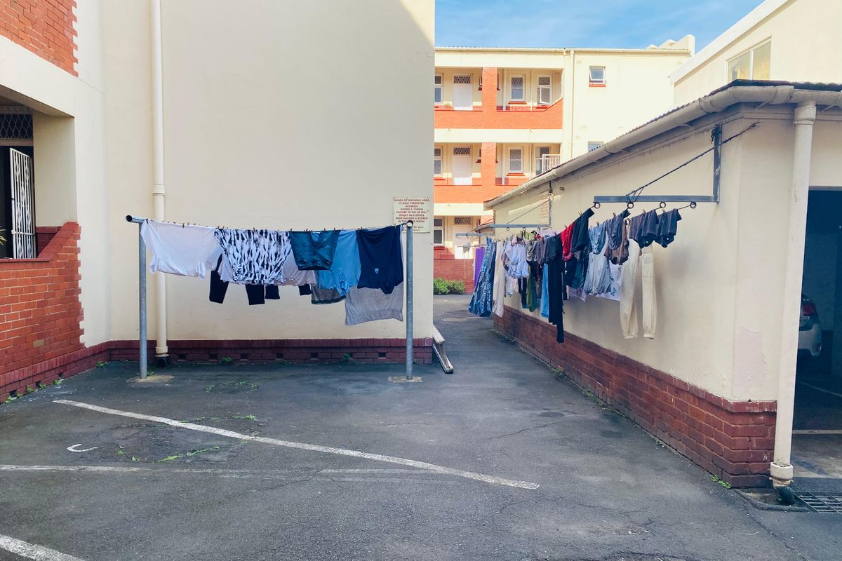 A communal outdoor drying area located between apartment building wings, featuring asphalt paving and fixed washing line infrastructure.