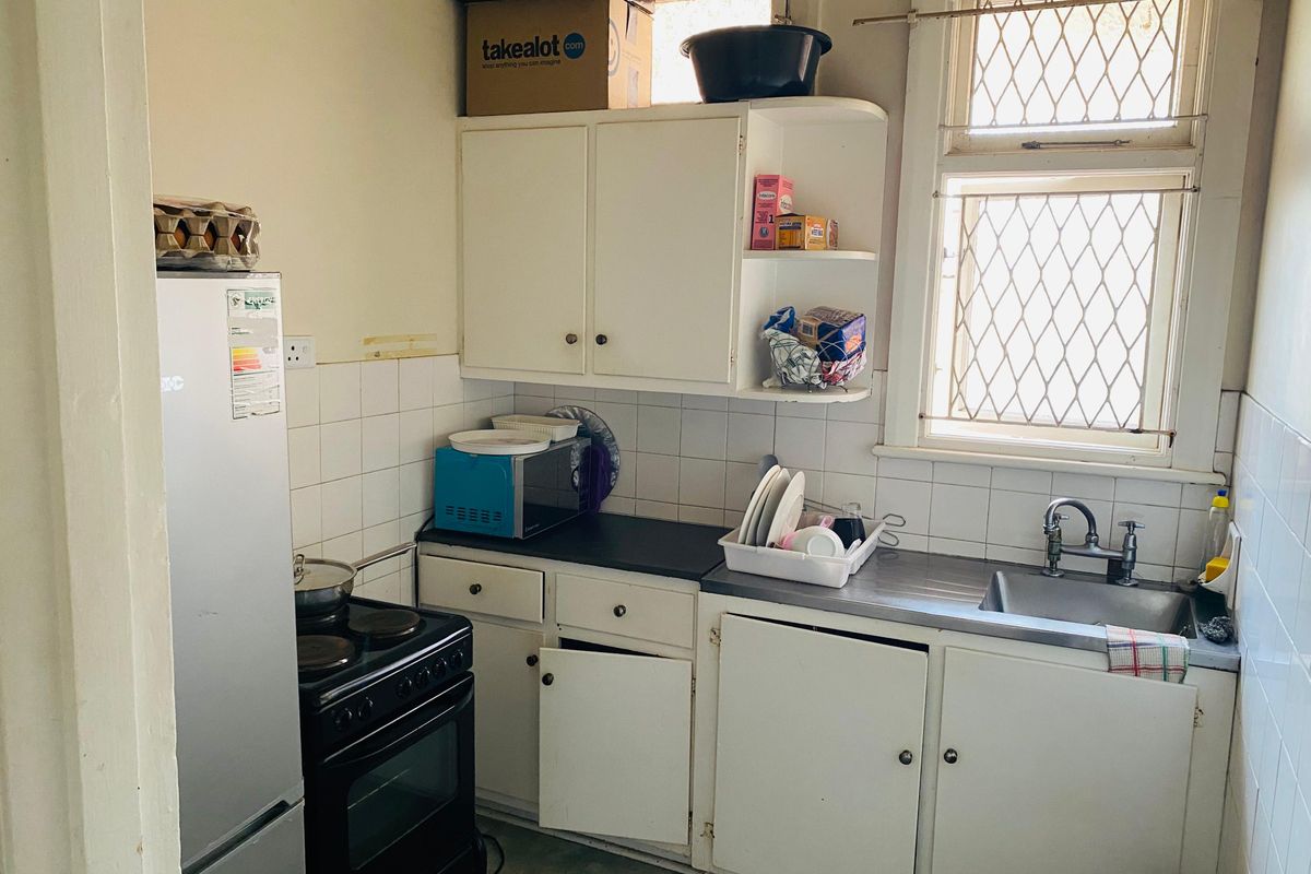 A compact, dated kitchen featuring original cabinetry, a stainless steel sink, and tiled splashbacks, offering significant potential for modernization and renovation.
