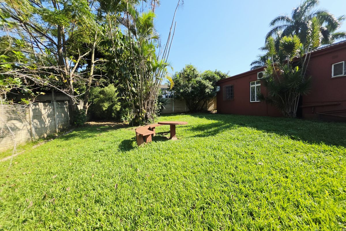 A spacious rear garden featuring a well-maintained lawn, mature trees, and a concrete boundary wall, providing a private outdoor area.