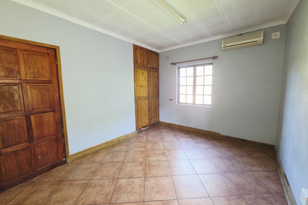 An empty bedroom featuring tiled flooring, built-in wooden cupboards, and an installed air conditioning unit.