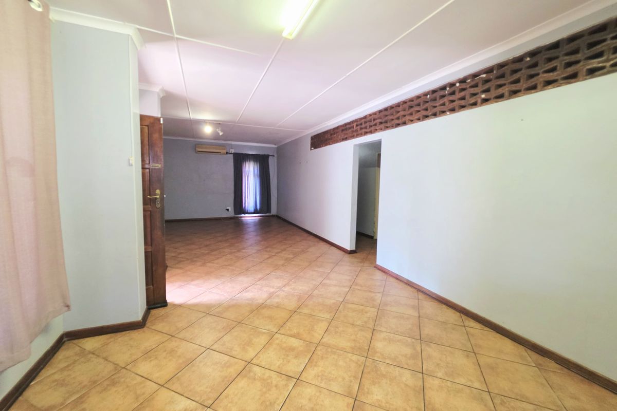 Spacious, empty living area featuring ceramic tile flooring, an air conditioning unit, and unique decorative breeze block wall detailing.