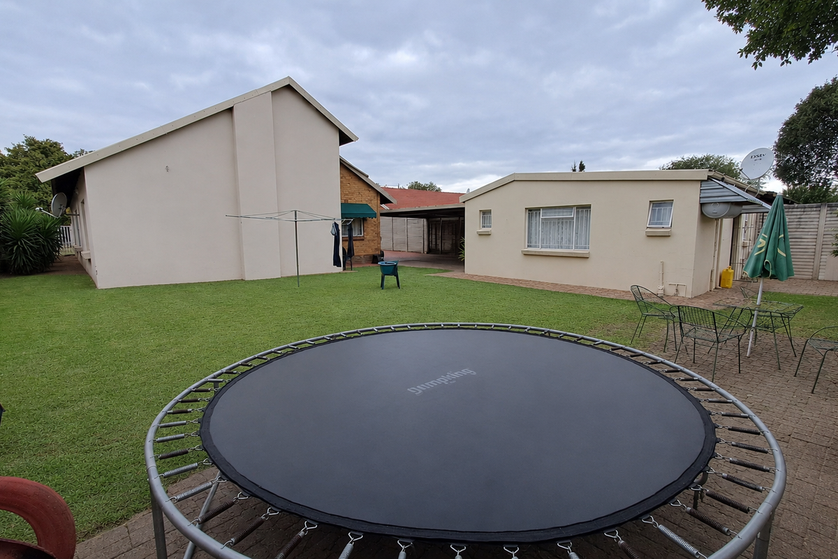 A spacious rear garden featuring a paved patio area, well-maintained lawn, and boundary walling, providing a functional outdoor space for the property.
