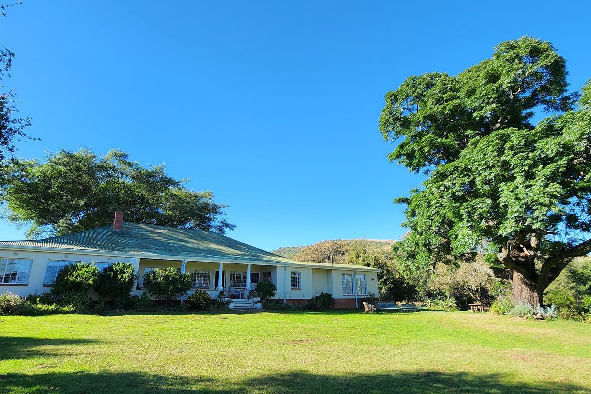 A view of the rear elevation of the farmhouse featuring a covered veranda, corrugated iron roof, and expansive garden with mature trees.
