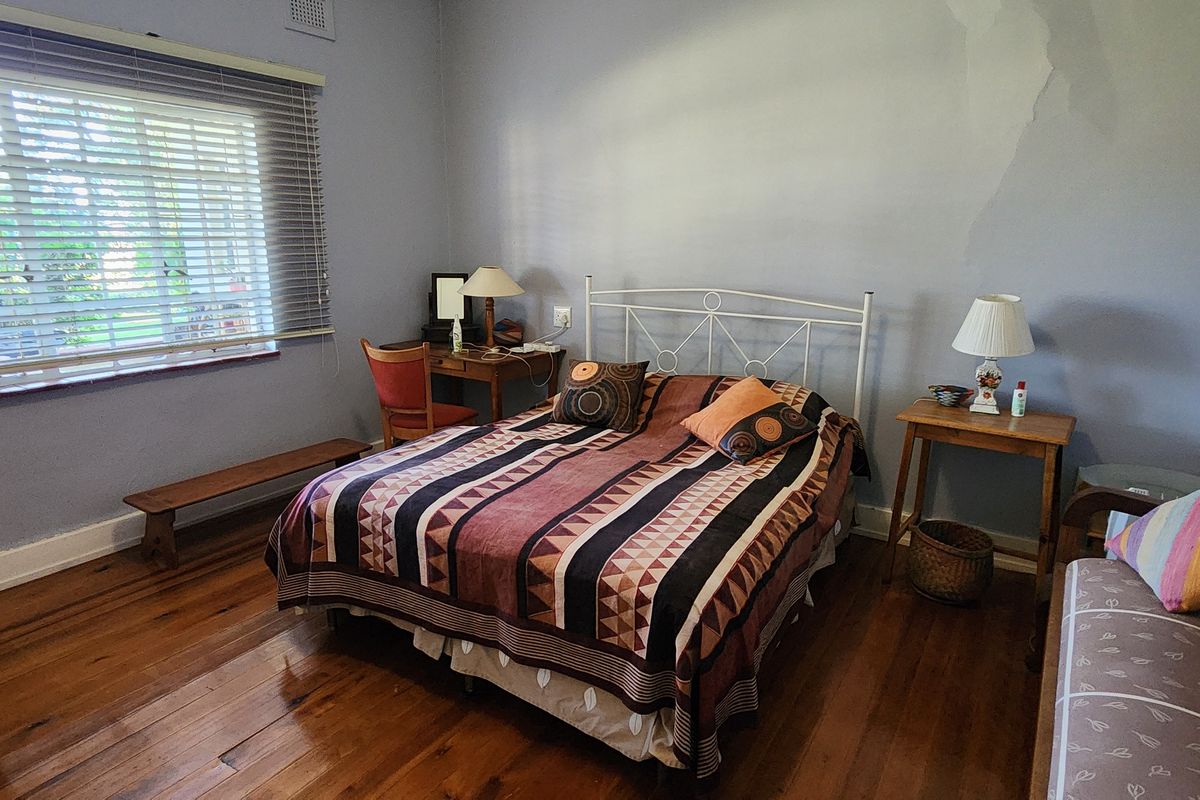 A bedroom featuring polished hardwood flooring and a large window with venetian blinds, requiring minor cosmetic attention to the wall finish.