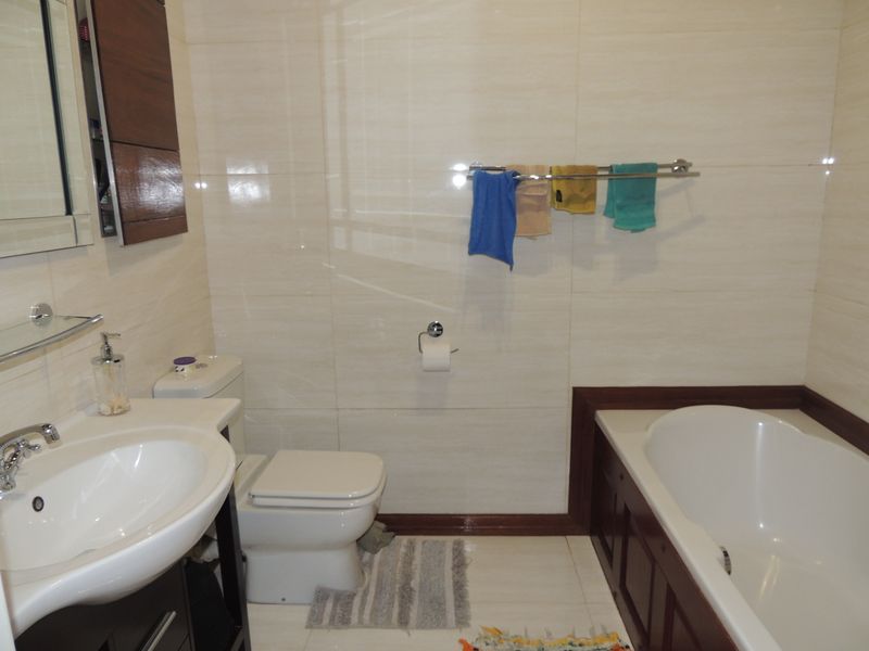 A well-maintained bathroom featuring a built-in vanity, ceramic basin, toilet, and a tiled bathtub surround with neutral wall tiling.