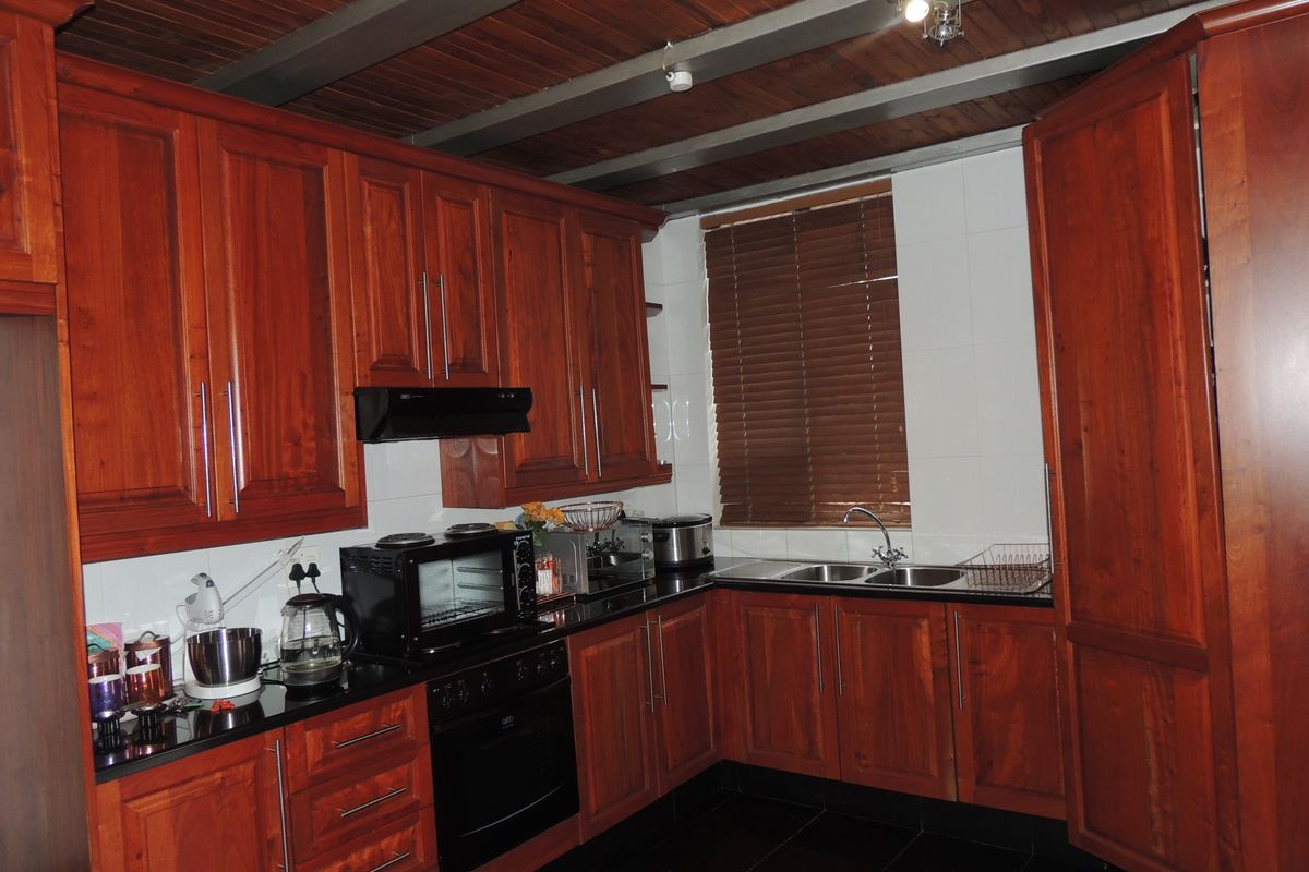 A functional kitchen featuring warm-toned wooden cabinetry, granite countertops, built-in oven, extractor fan, and exposed wooden ceiling beams.
