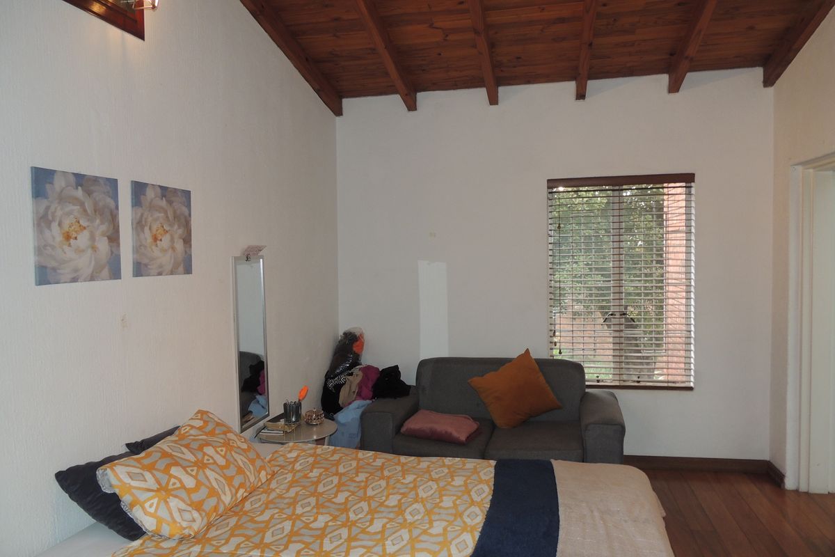 A bedroom featuring exposed timber ceiling beams, hardwood flooring, and a window with venetian blinds, offering a rustic aesthetic with potential for cosmetic updates.